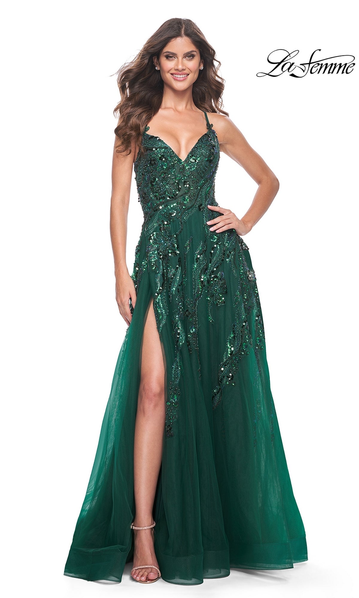Woman in an emerald La Femme Long A-Line Sequin-Print Prom Dress 32346 with a thigh-high slit and spaghetti straps, posing against a white background with wavy brown hair.